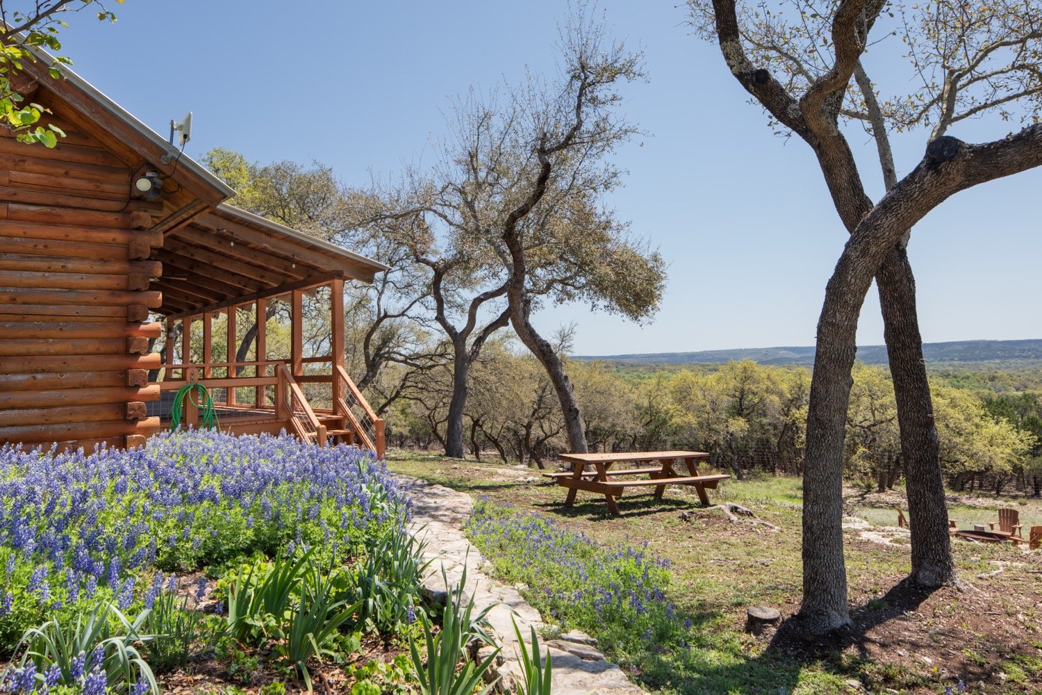 Vesper Lodge cabin with bluebonnets in bloom and the Hill Country beyond