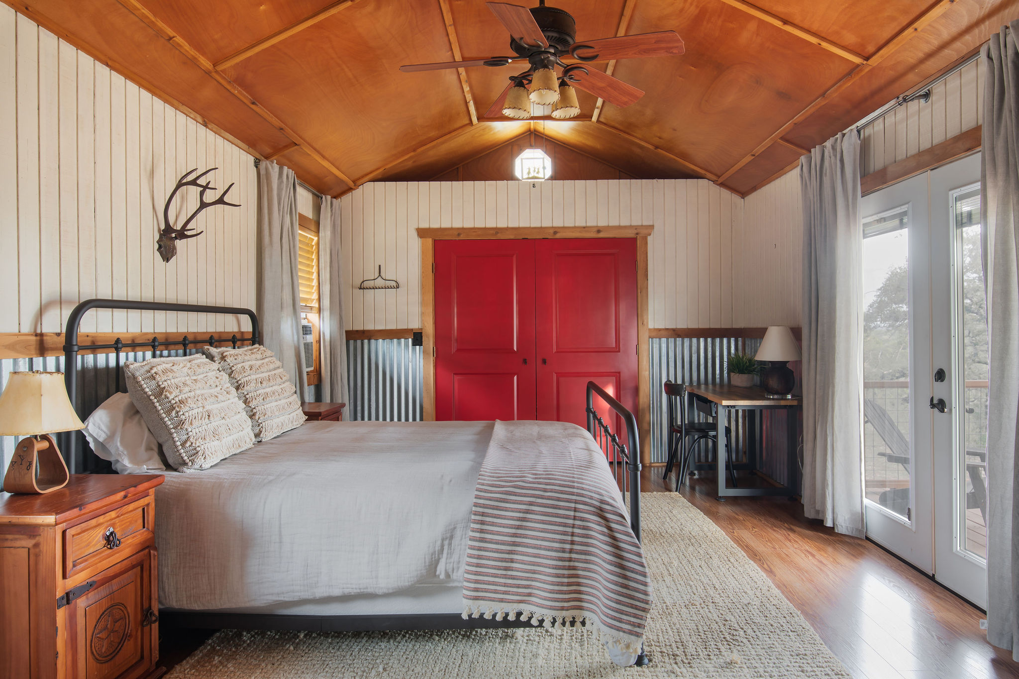 The back cabin bedroom — an iron bed, red doors, and French doors onto the deck